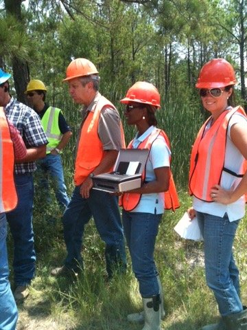 Team members in hard hats and safety vests during a field visit among the pines