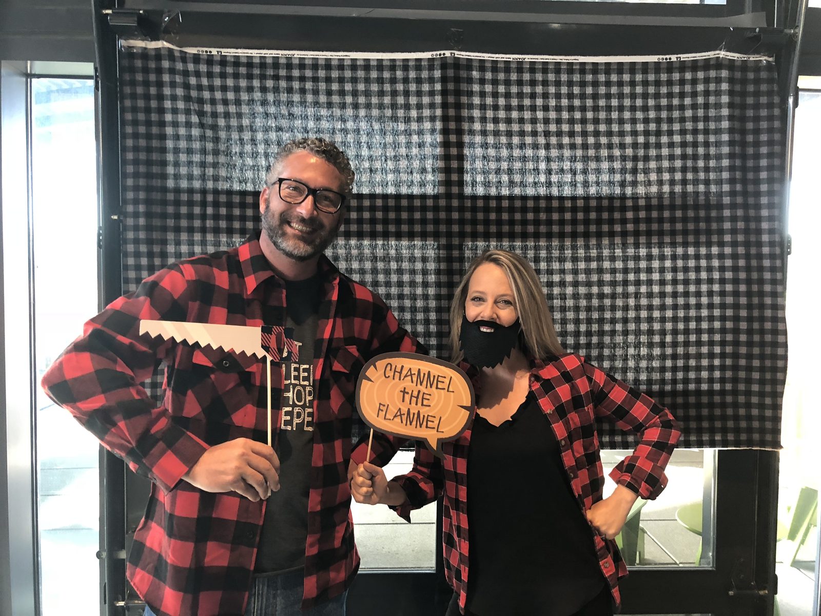 Two colleagues in red flannel at a photo-booth backdrop holding a Channel the Flannel sign